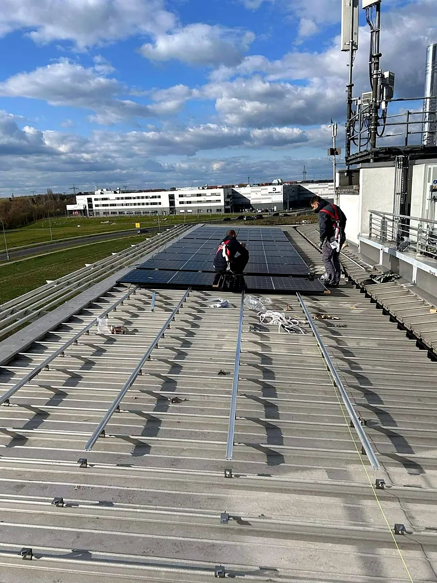 Dvojica montera s pojasevima postavljaju solarne panele na krov hale